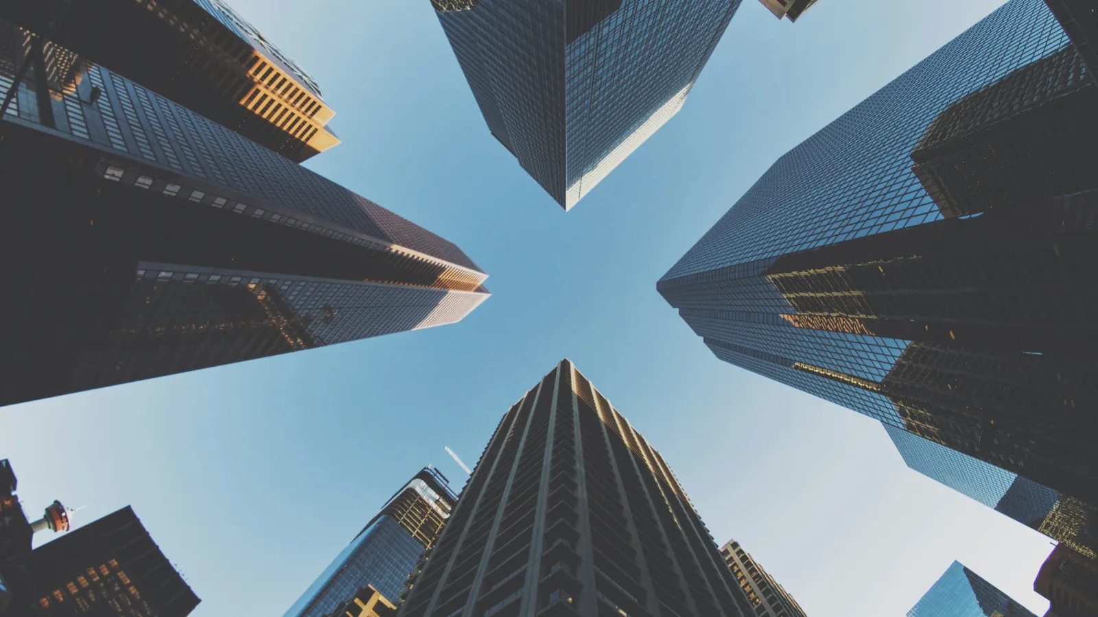 Upward view of tall modern skyscrapers converging against a clear blue sky in a city center.