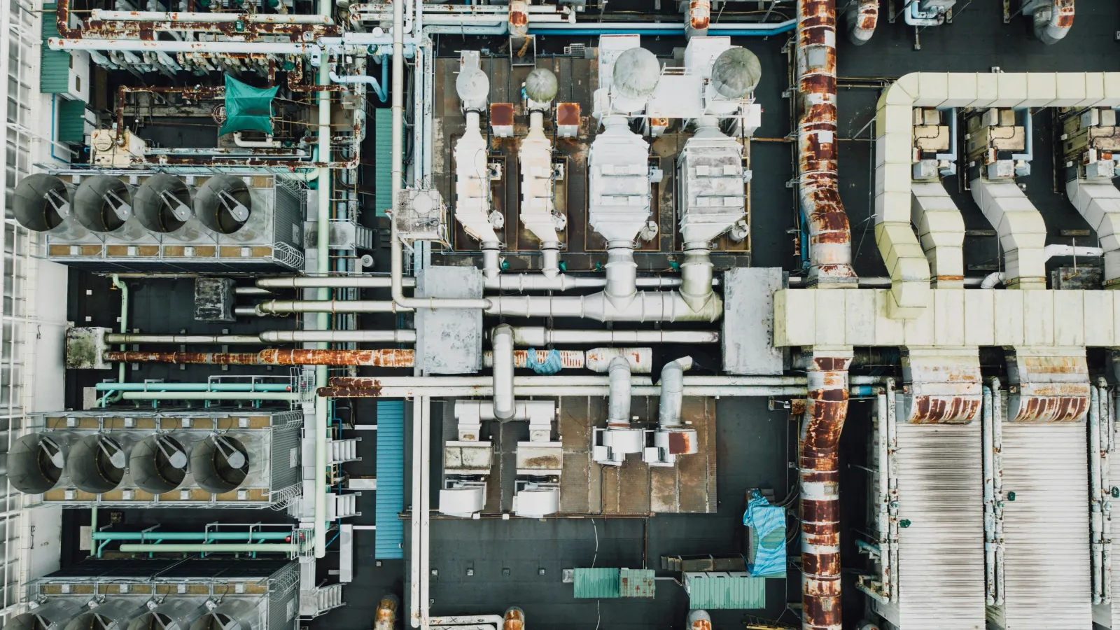 Aerial view of an industrial rooftop with rusty pipes, ventilation units, and complex machinery layout.