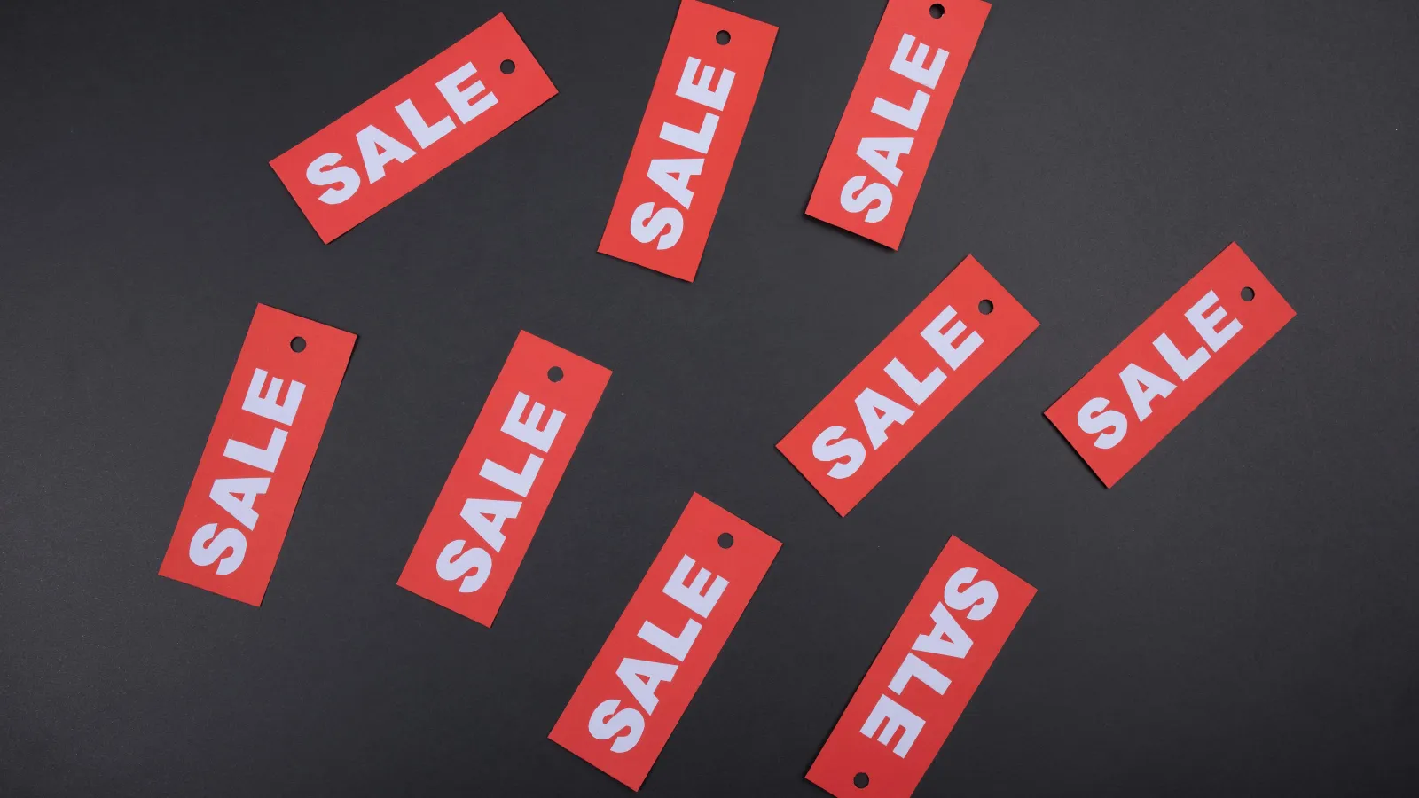 Multiple red sale tags with white text scattered on a black background indicating discounts and promotions.