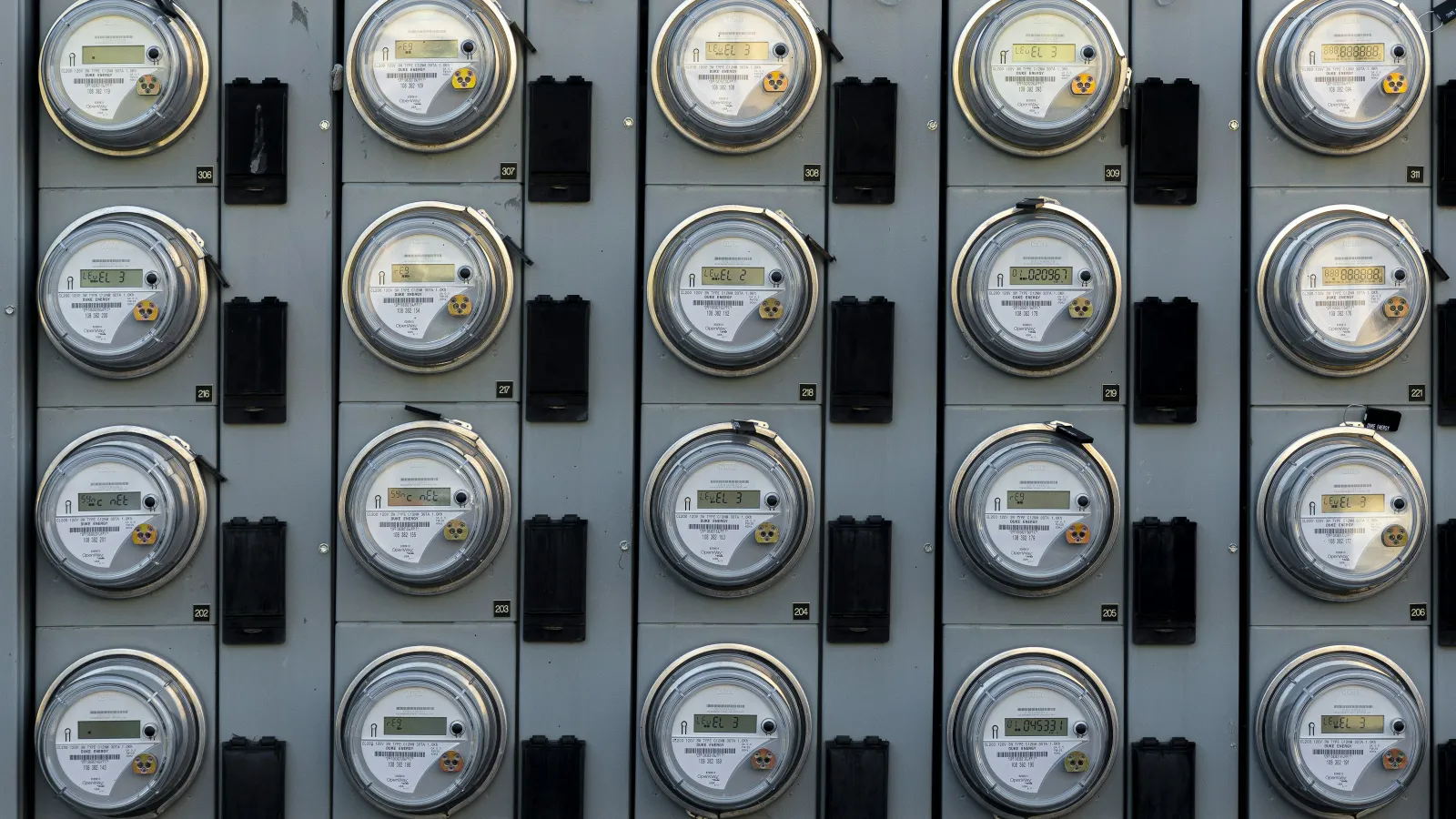 Multiple electric meters arranged in a grid on a gray panel measuring electricity usage.