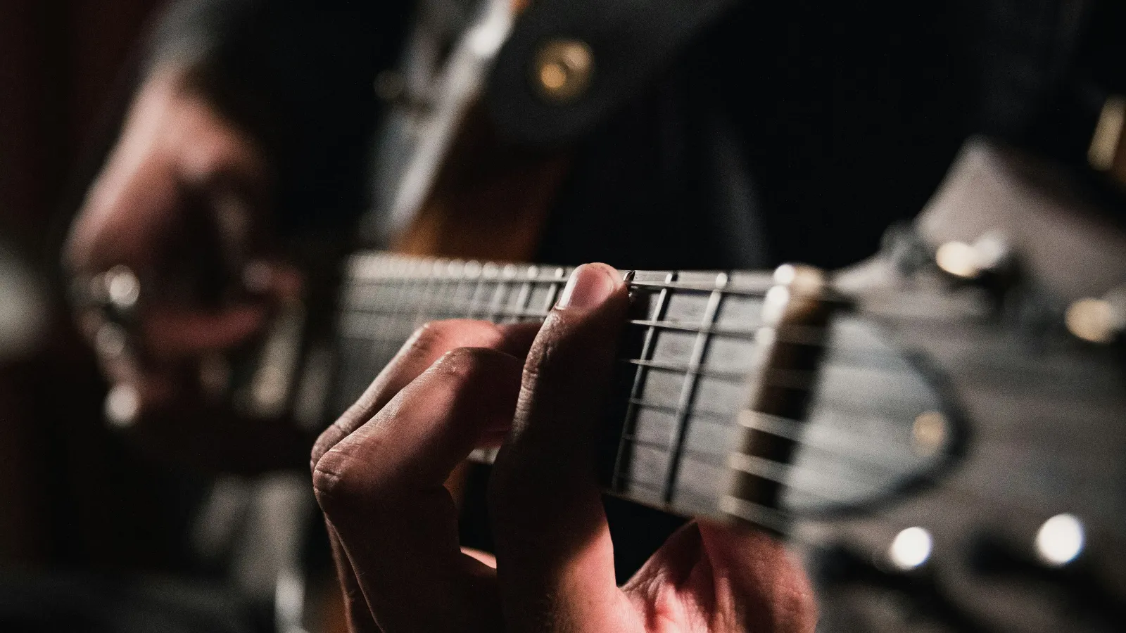 Close-up of a person playing an electric guitar, focusing on fingers pressing the strings on the fretboard.