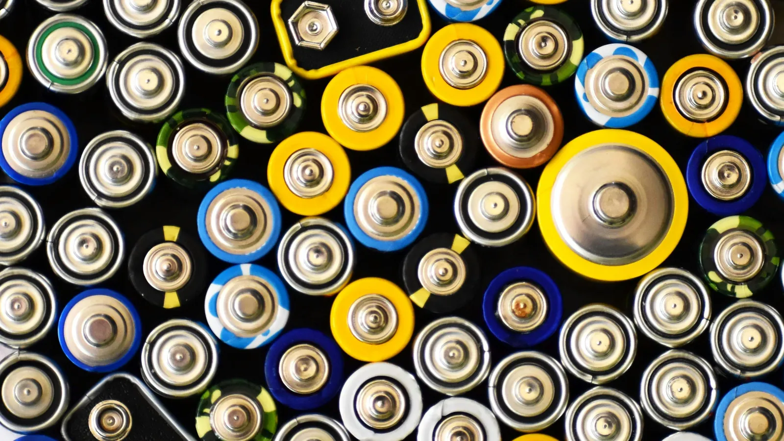 Top view of assorted batteries showing positive terminals with various sizes and colors densely arranged.
