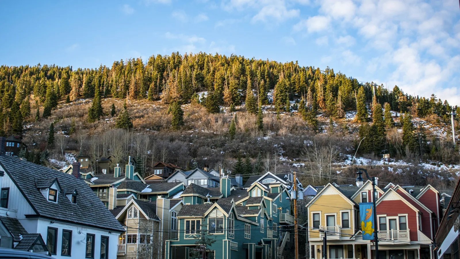 Colorful houses at the base of a forest-covered hill under a partly cloudy blue sky during daytime