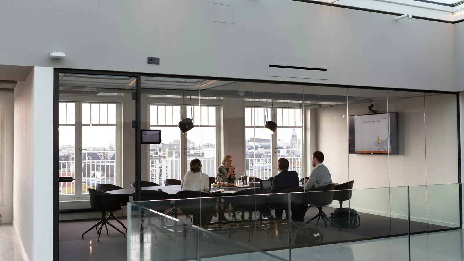 Four business professionals having a meeting inside a modern glass-walled conference room with city views.