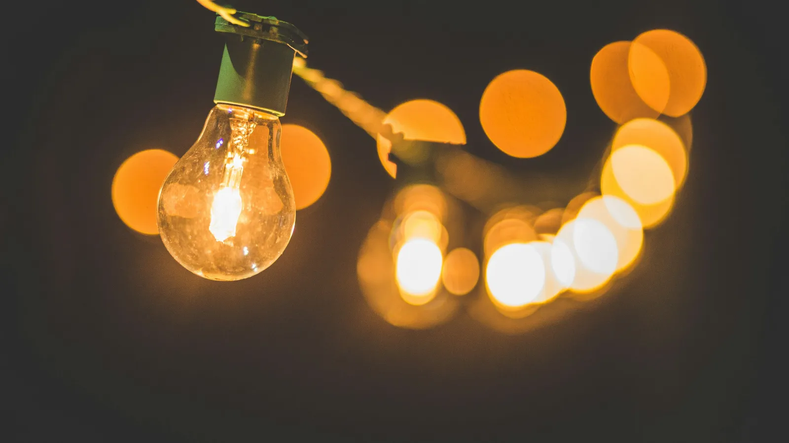 Close-up of a glowing incandescent bulb with warm bokeh lights in the background on a dark backdrop