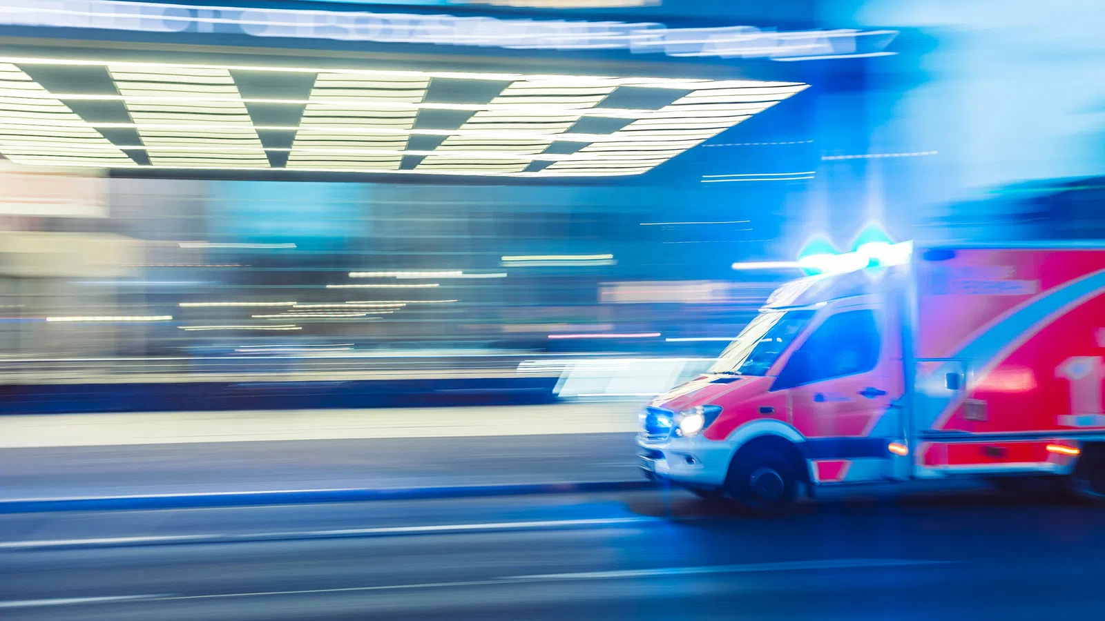 Emergency ambulance with flashing lights speeding through a city street at night with motion blur effect