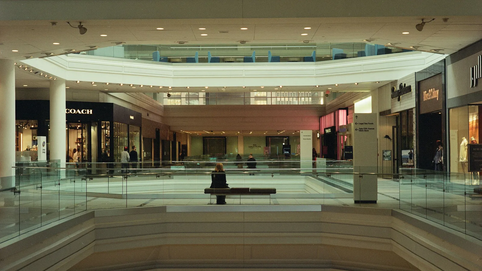Interior of a modern multi-level shopping mall with glass railings and people walking on tiled floors.