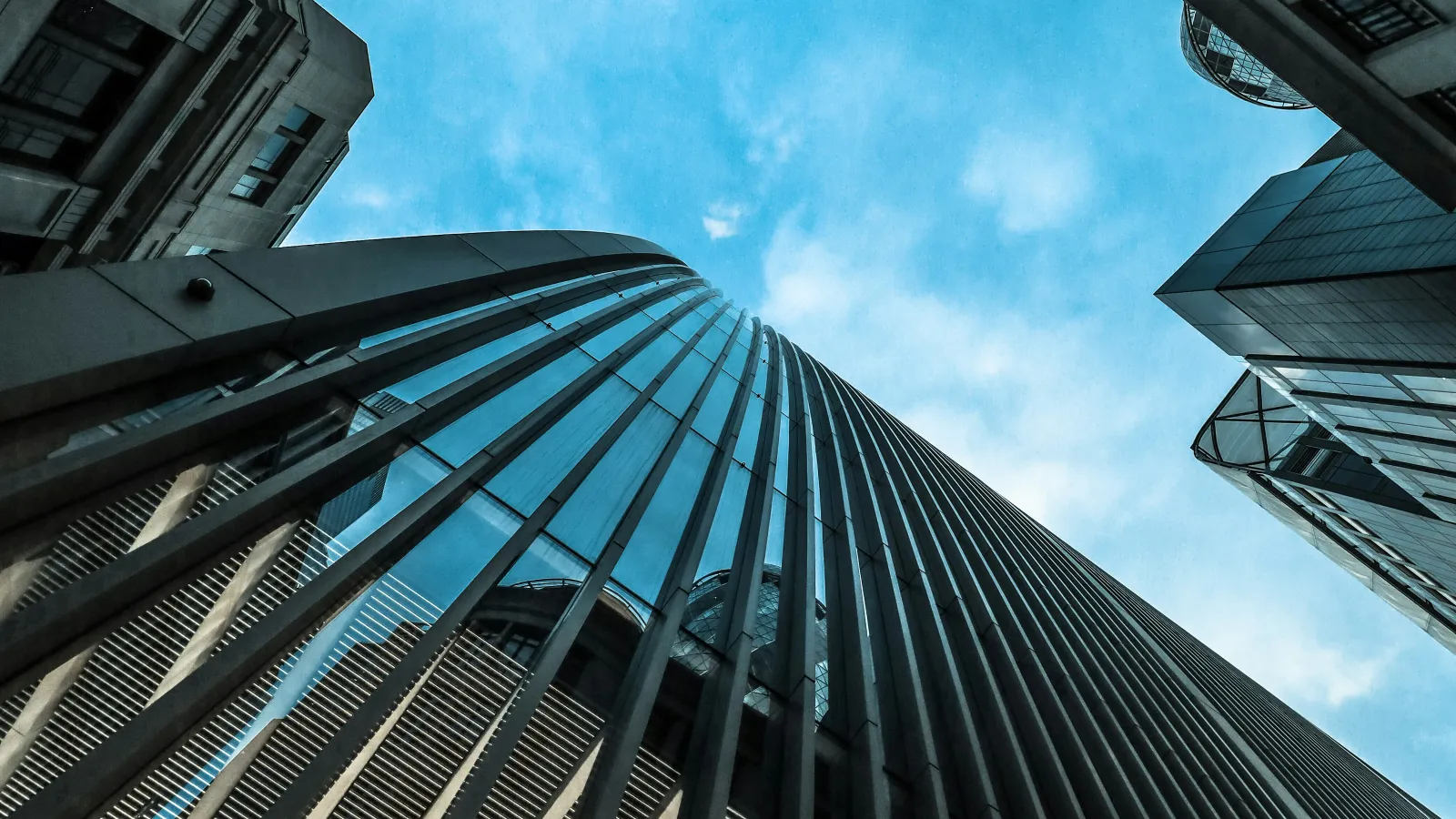 Upward view of modern skyscrapers with glass and metal facades against a blue sky with clouds.