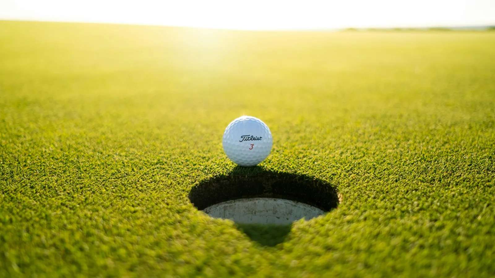 Golf ball on the edge of a hole on a sunlit green golf course