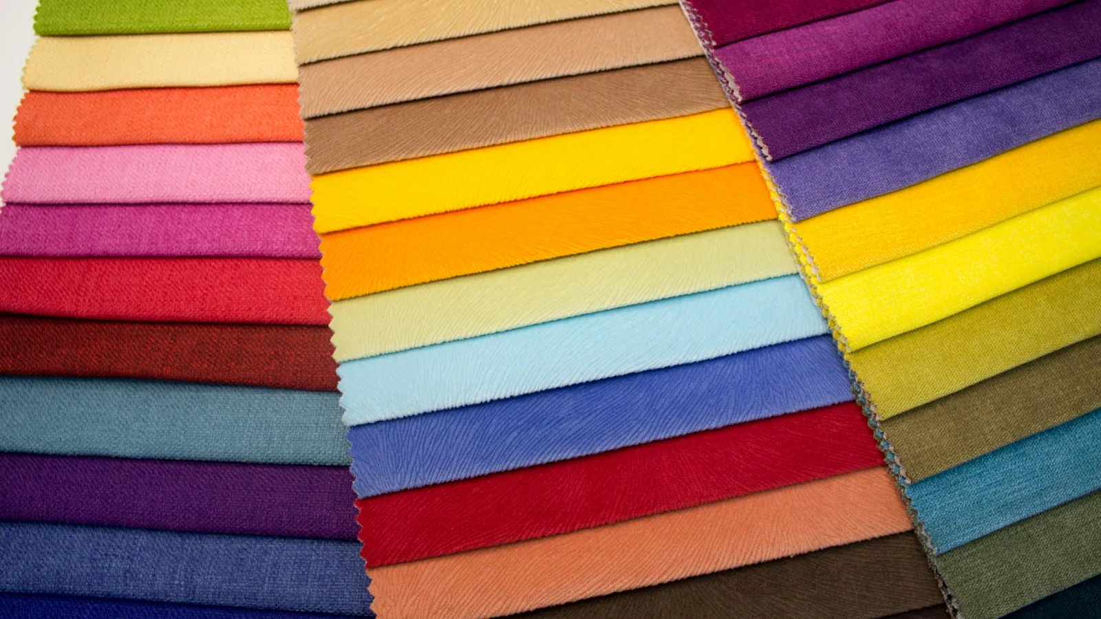 Colorful fabric swatches arranged in overlapping rows showcasing diverse vibrant shades and textures.