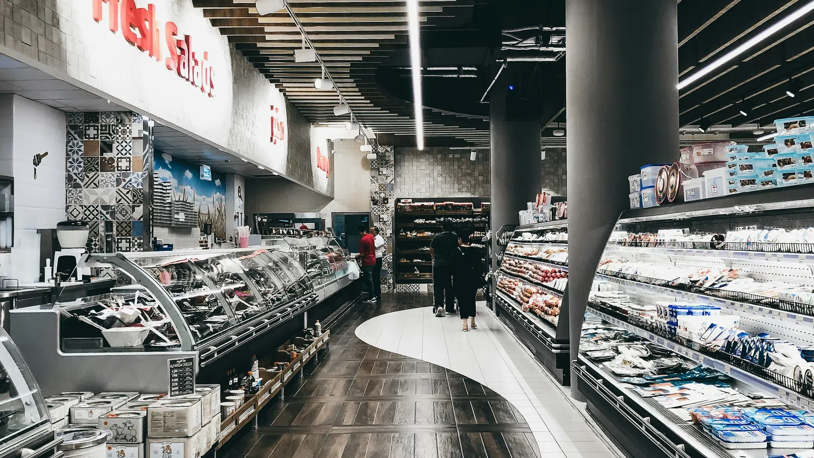Modern supermarket interior with curved wood and tile flooring and fresh salad counters on the left side.