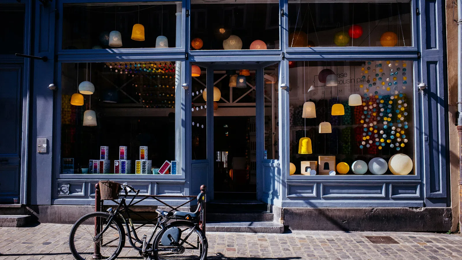 Front view of a stylish lighting store with colorful hanging lamps and a bicycle parked outside on the street.