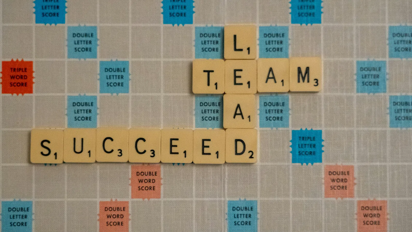 Scrabble tiles spelling team and succeed on a score multiplier board for word game strategy.