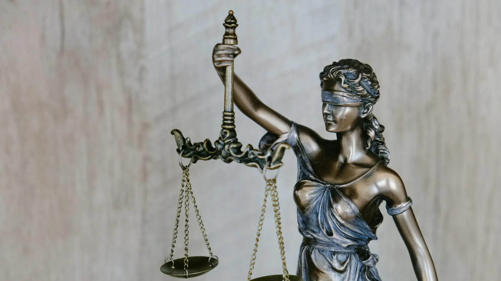 Bronze statue of blindfolded Lady Justice holding balanced scales against a blurred wooden background