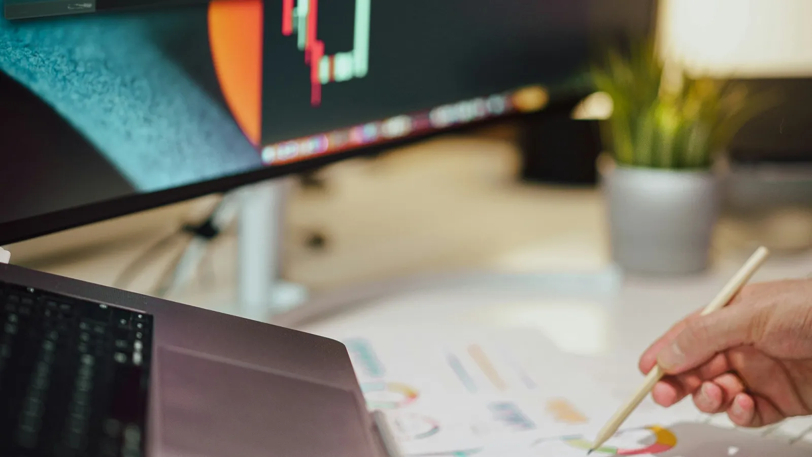 Person analyzing financial charts on computer screen and printed graphs with calculator on desk.