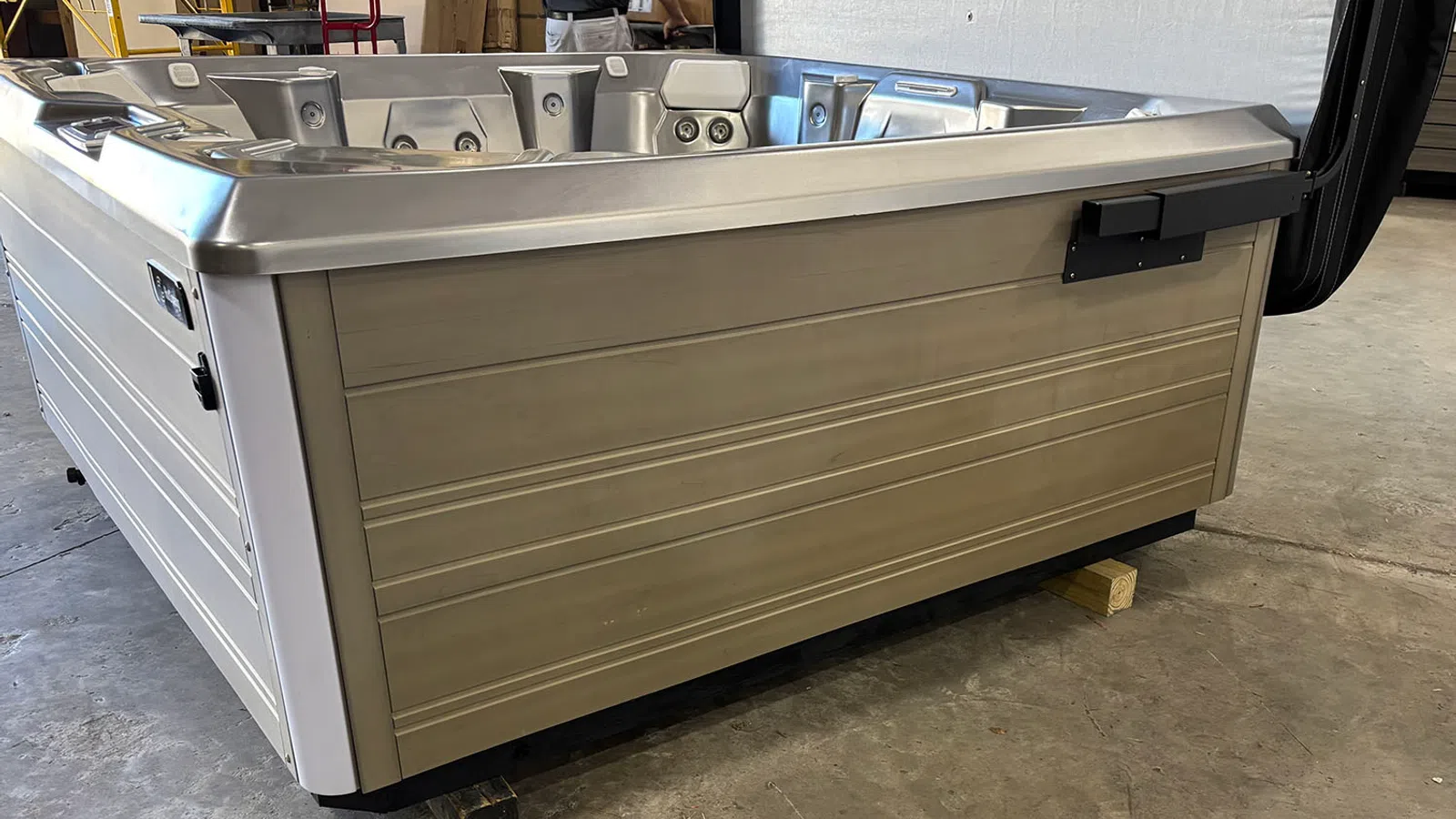 Modern rectangular outdoor hot tub with stainless steel finish on warehouse floor, view of side panel and jets.