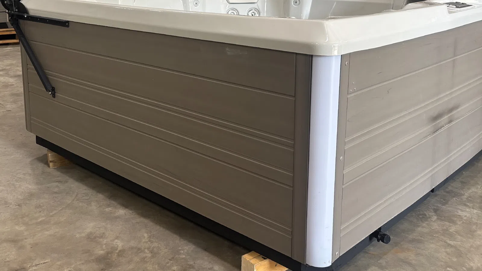 Corner view of a beige outdoor hot tub with a white rim and textured panels on a concrete floor.