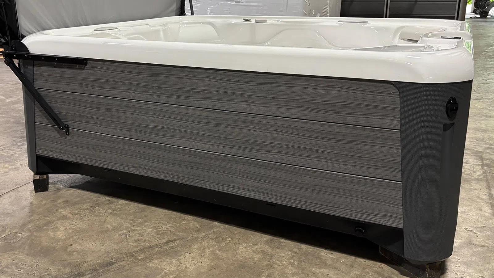 Modern gray and white outdoor spa hot tub with textured side panels on a concrete floor indoors.