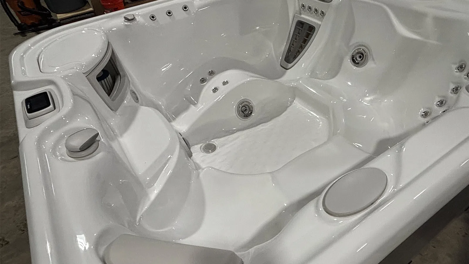 Empty white acrylic hot tub with multiple jet nozzles and contoured seating in an indoor setting.