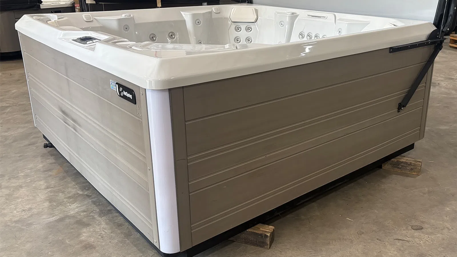 Large beige and white outdoor hot tub with multiple jets and seating, placed indoors on a concrete floor.