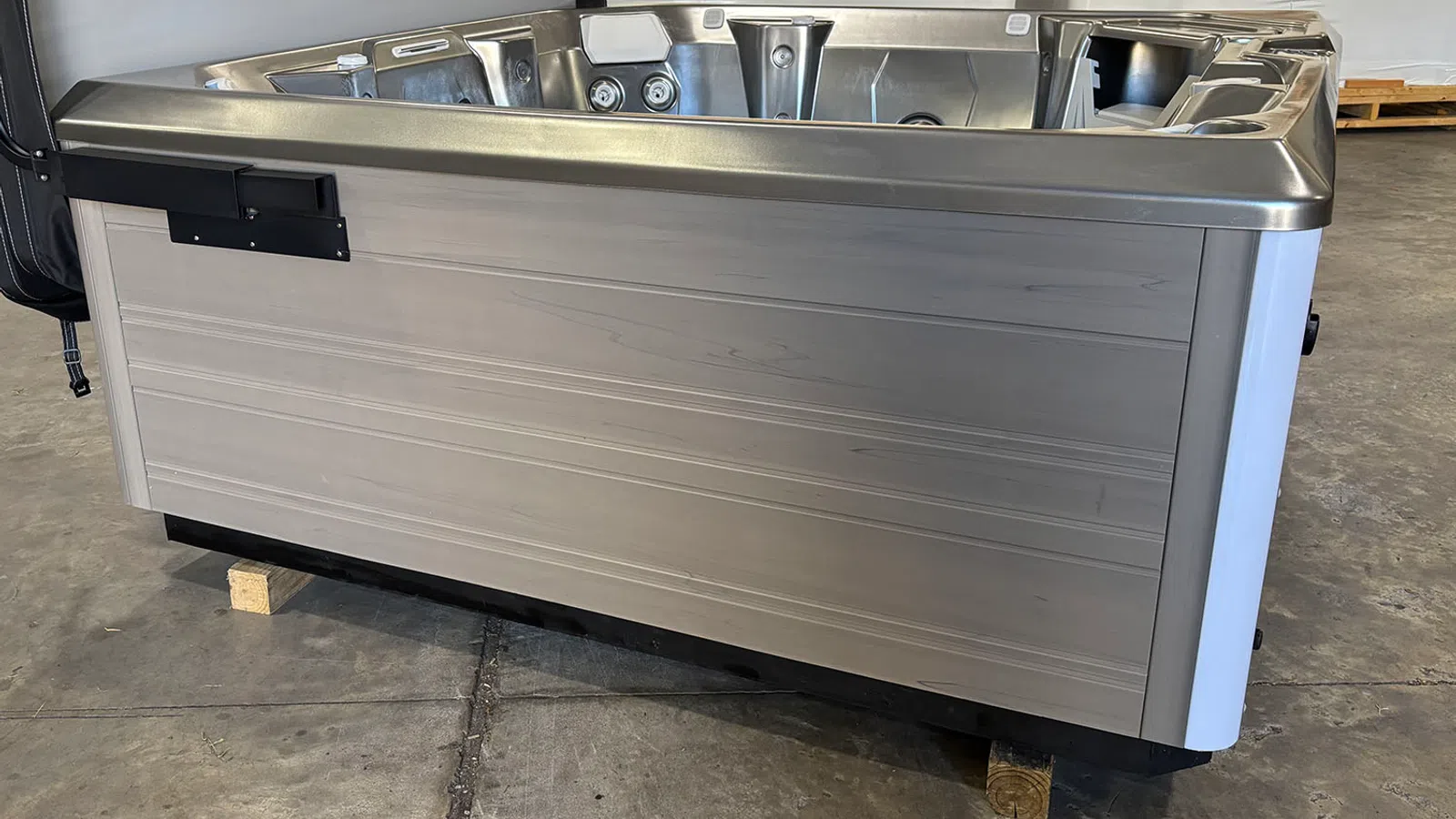 Modern hot tub with stainless steel trim set on warehouse floor, side view showing jets and seating inside