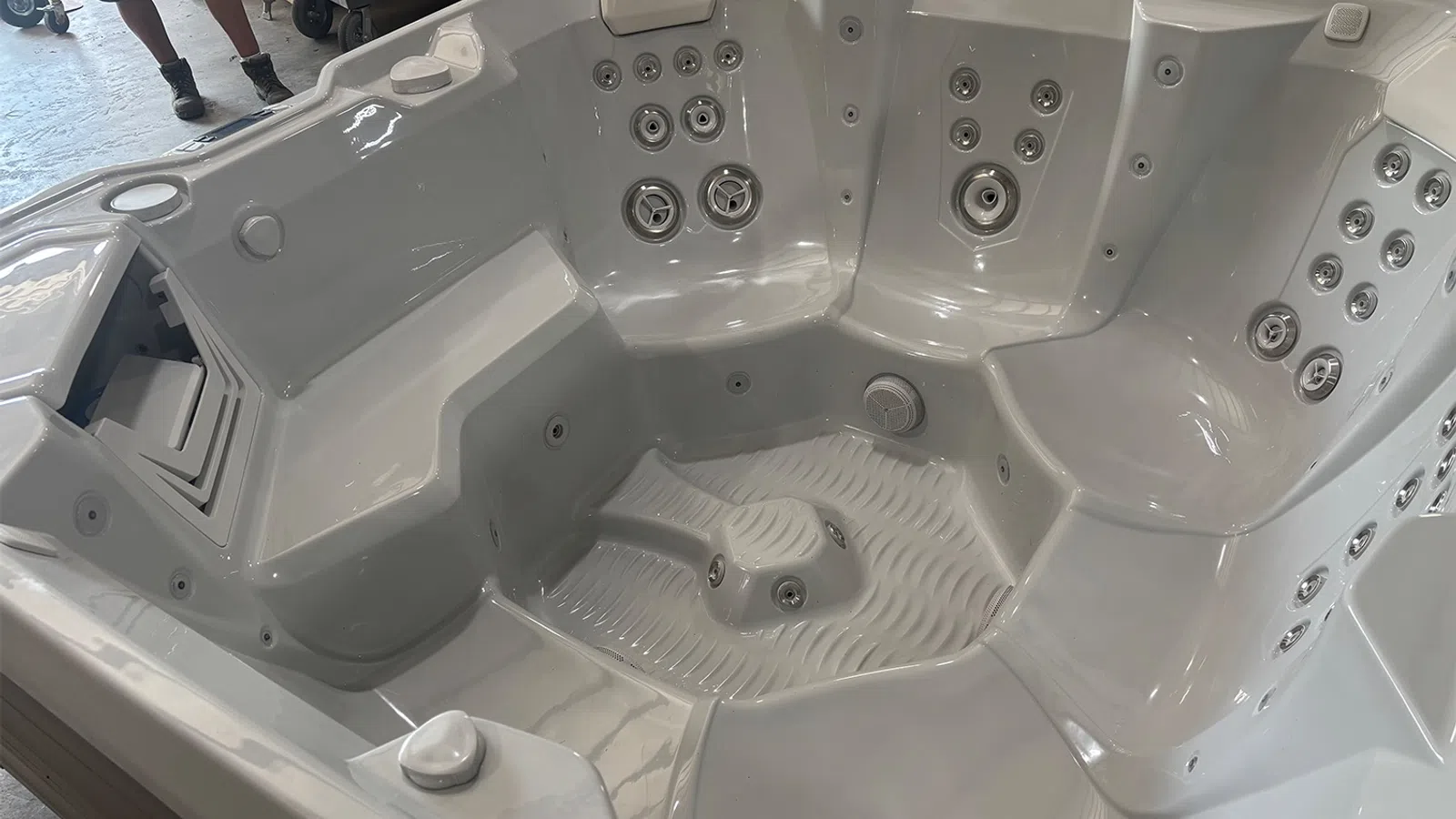 Empty white luxury hot tub with multiple jet nozzles and contoured seating inside a showroom.
