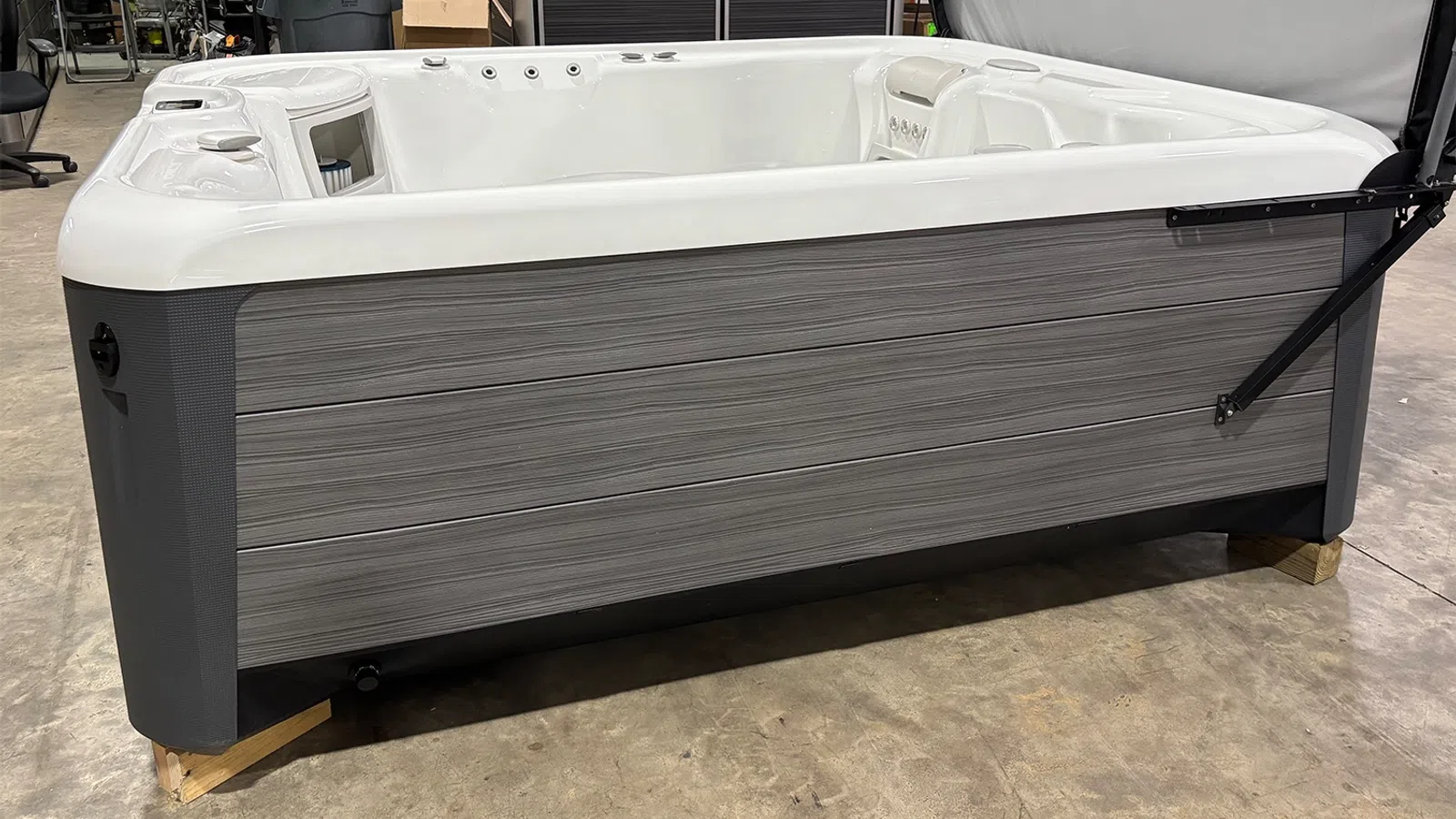 Modern rectangular outdoor hot tub with gray wood paneling and white interior in warehouse setting