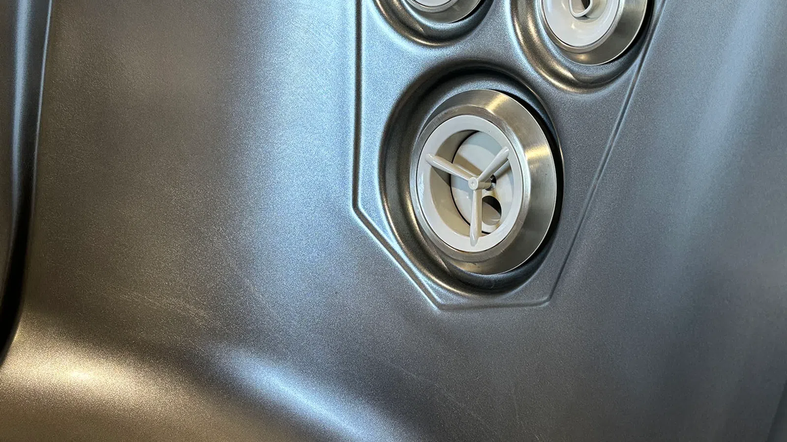 Close-up of silver metallic surface with three circular vents or control knobs in a triangular arrangement.