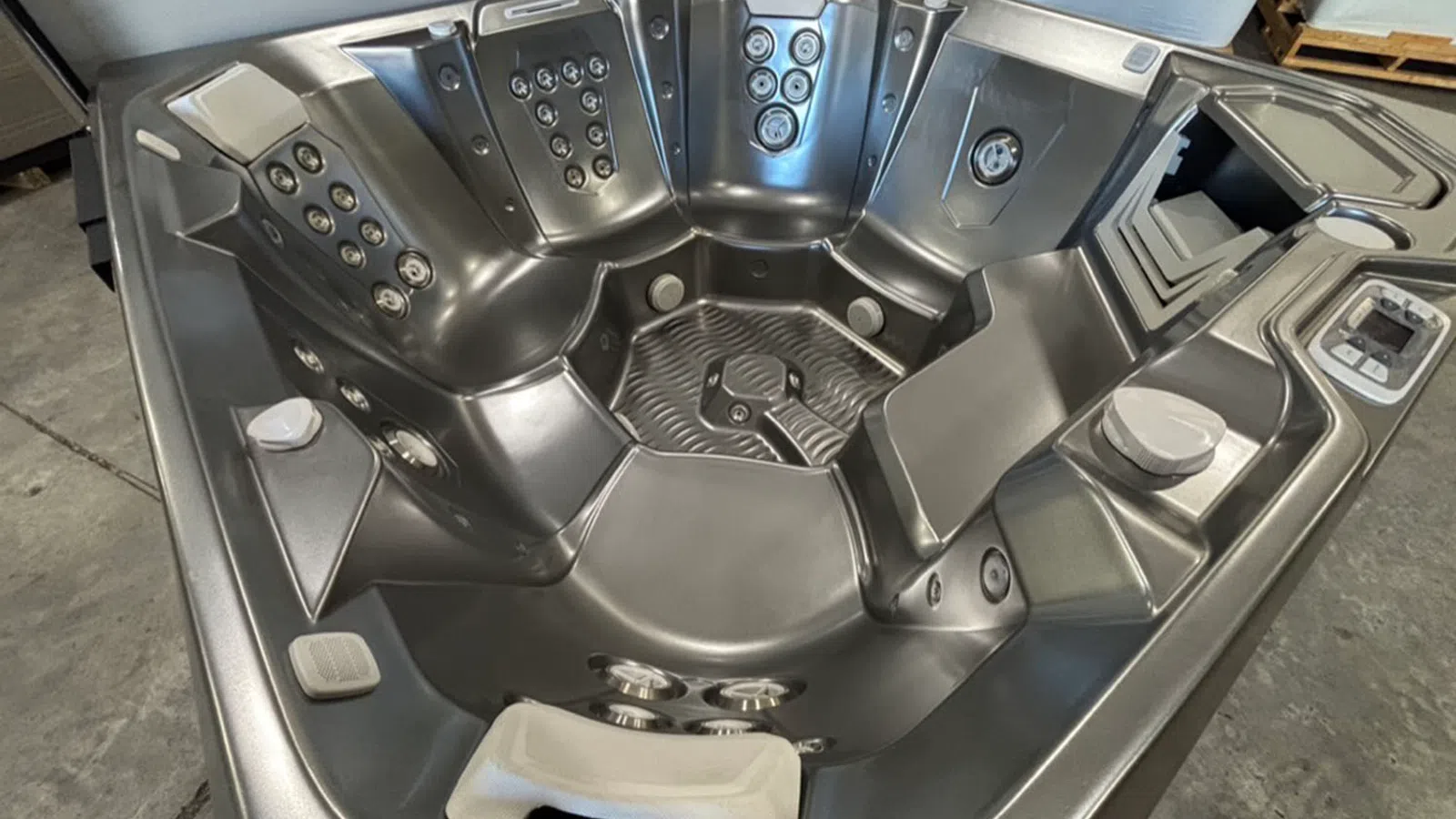 Modern gray hot tub with multiple seating areas and built-in jets in an indoor warehouse setting.