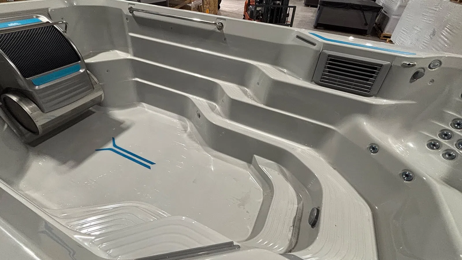 Empty white modern hot tub with built-in seating, headrest, and jets in a showroom setting.
