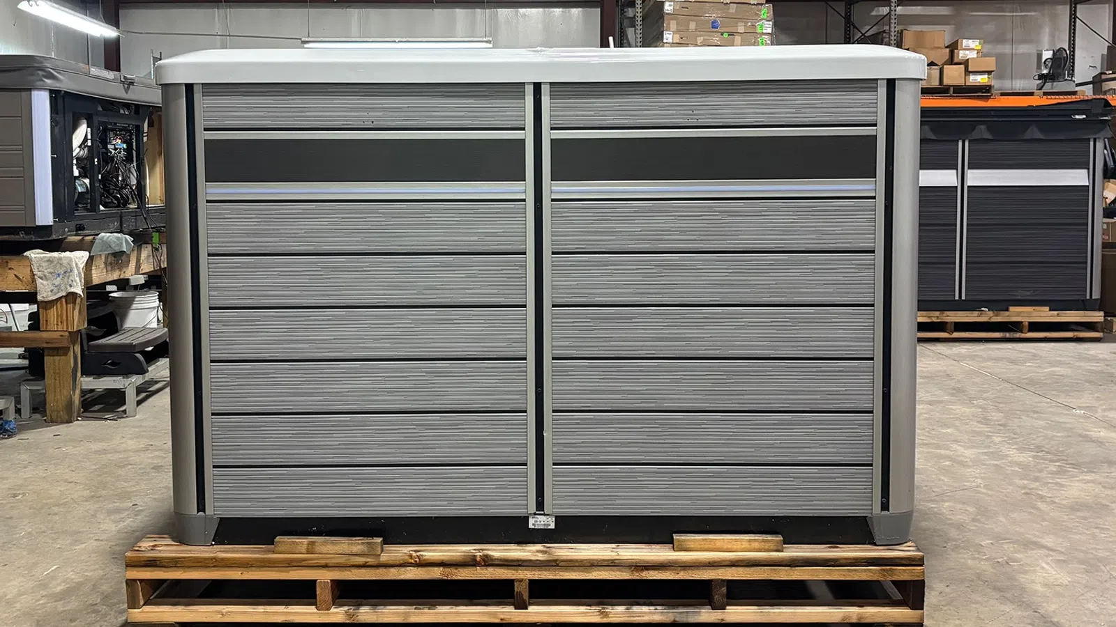 Large gray outdoor storage shed with horizontal panels on wooden pallet inside warehouse.
