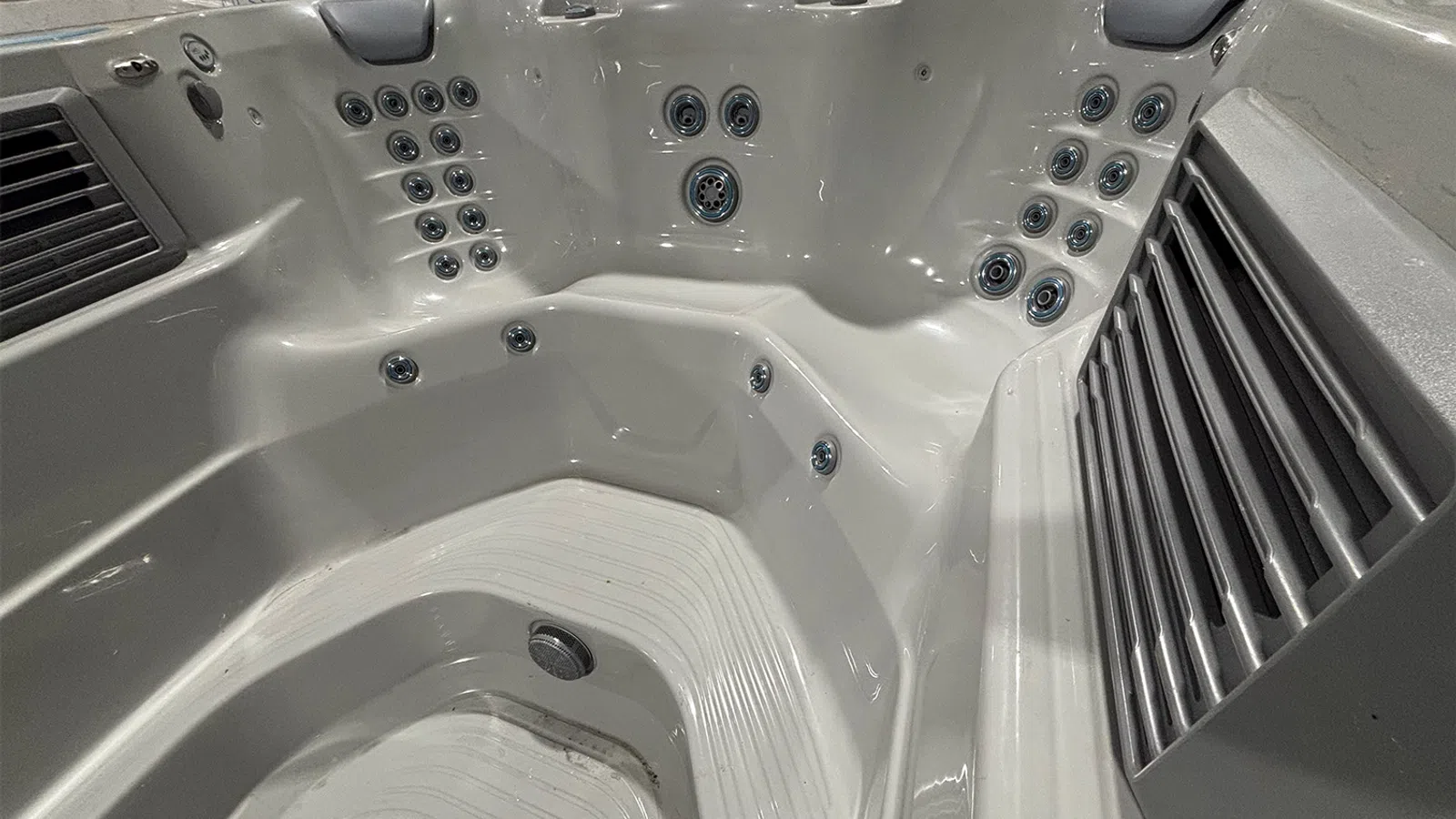 Close-up of an empty white hot tub with multiple massage jets and ergonomic seat contours.