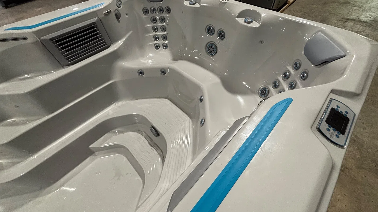 White modern hot tub with blue accents, multiple jets, ergonomic seats, and digital control panel in indoor setting.
