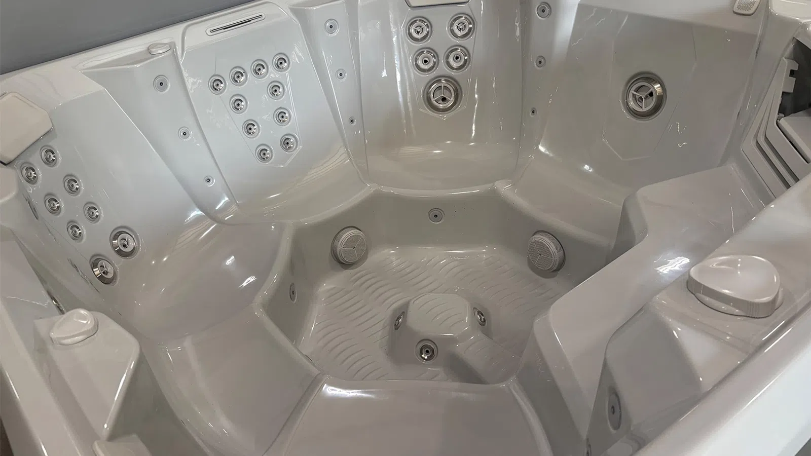 Interior view of a white multi-seat hot tub with numerous water jets and ergonomic seating.
