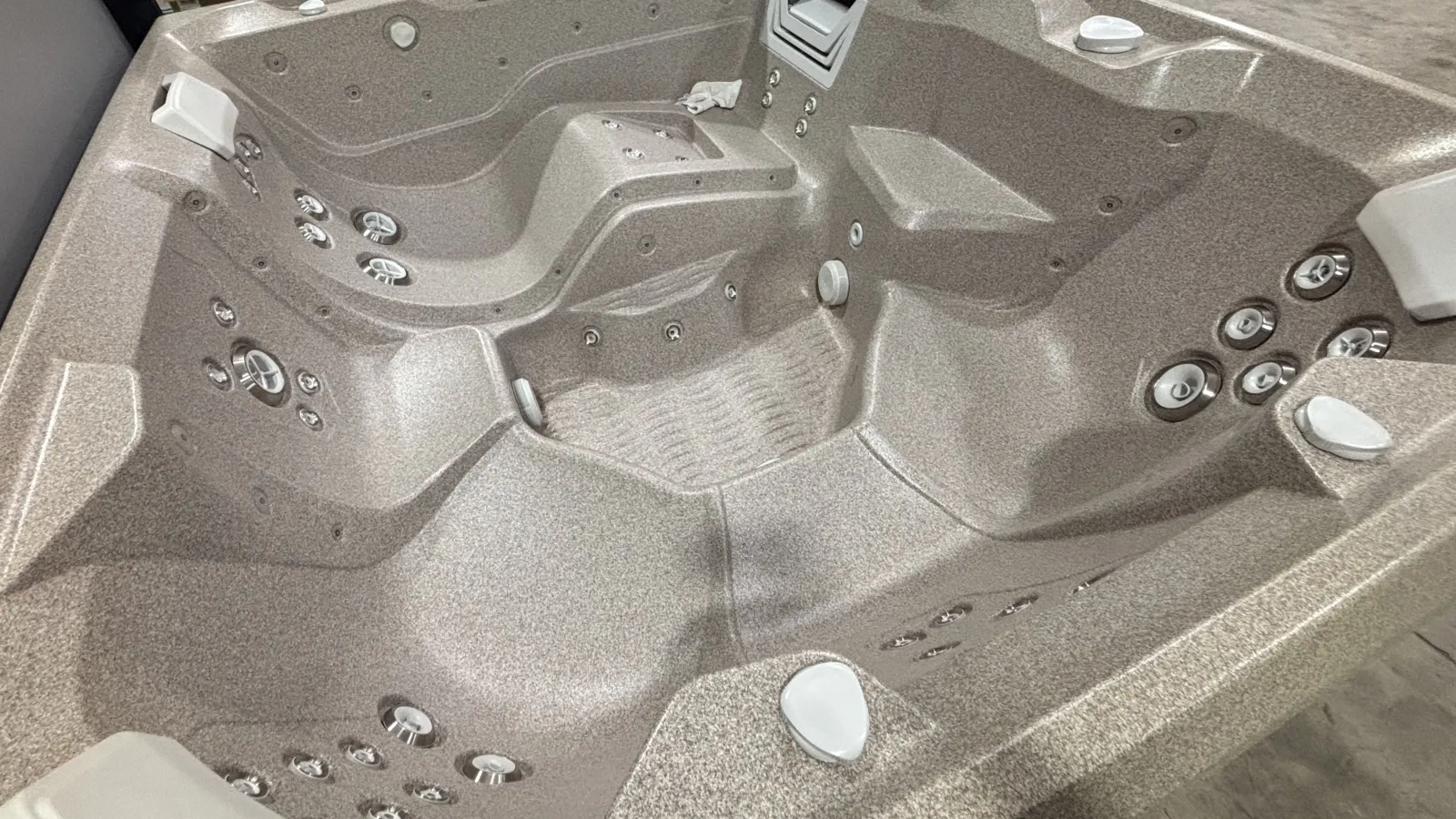 Empty modern hot tub with multiple ergonomic seats, jet nozzles, and headrests in a neutral tone finish.