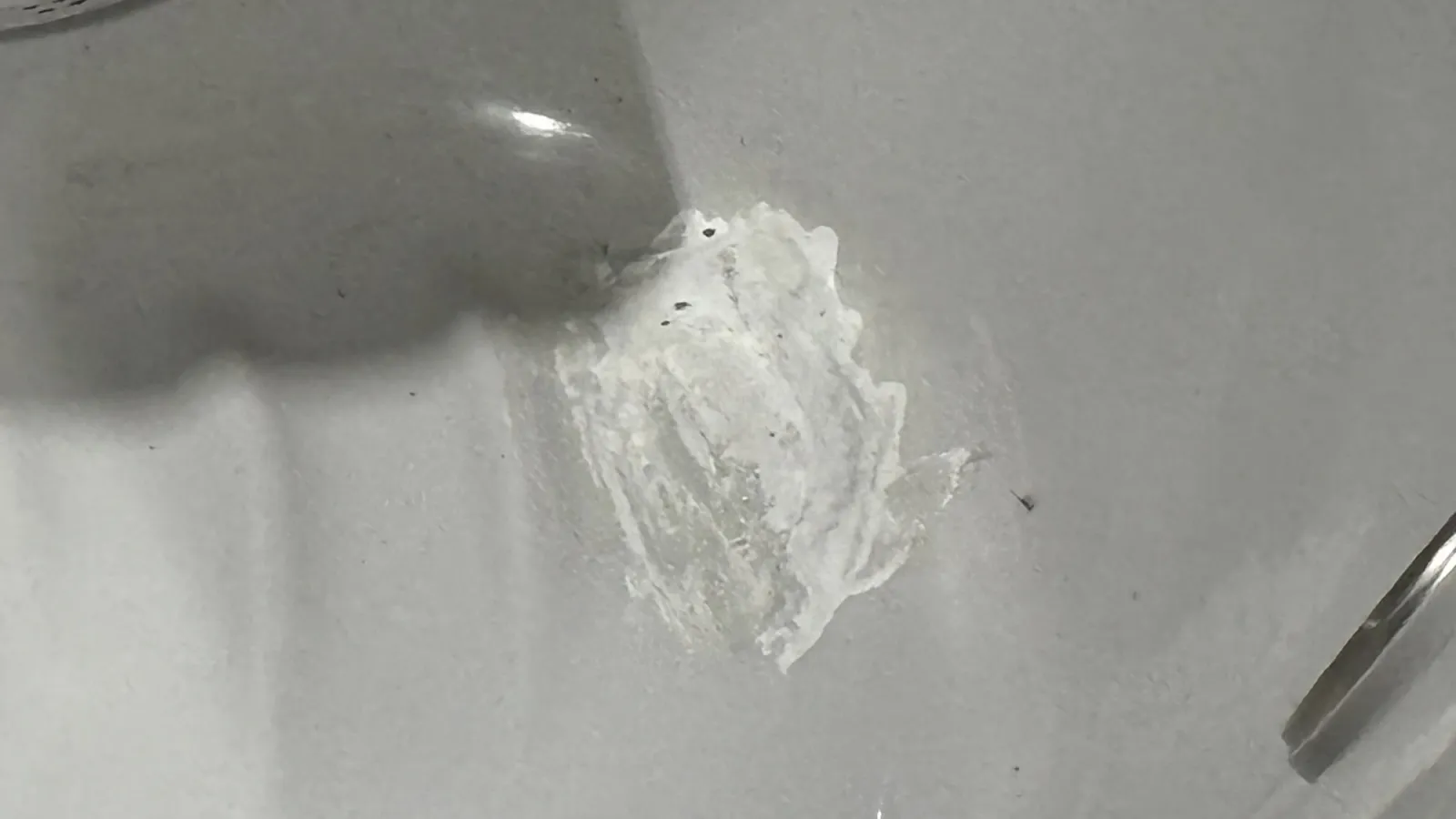 Close-up of a gray surface with a white paint or plaster patch and a metal object edge.