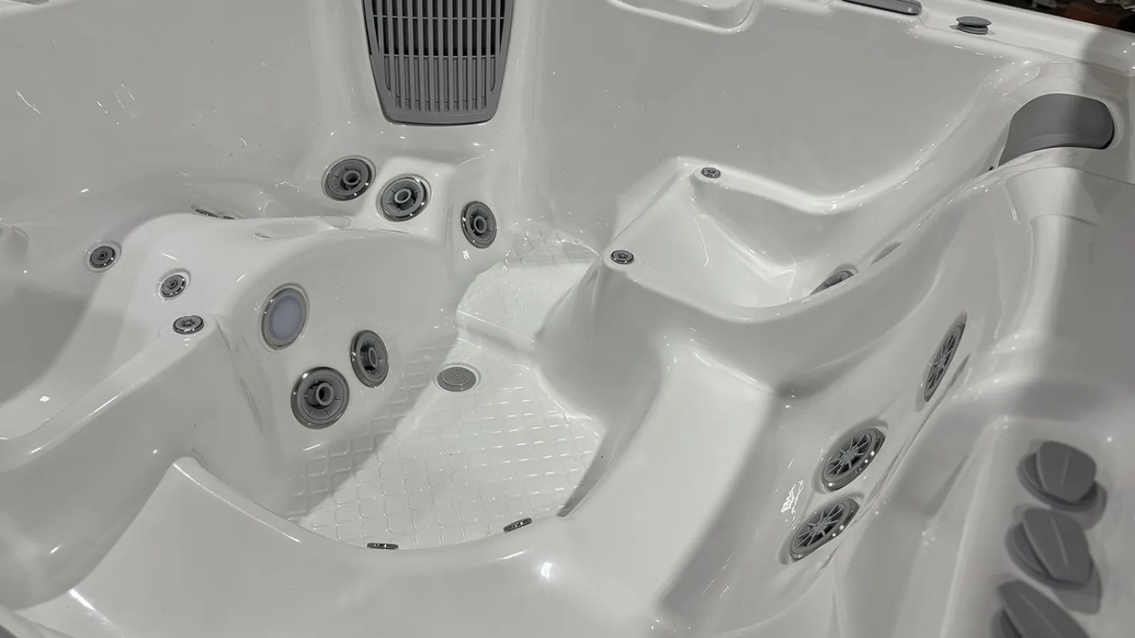 White indoor hot tub showing multiple water jets, seating areas, and control knobs inside the tub.