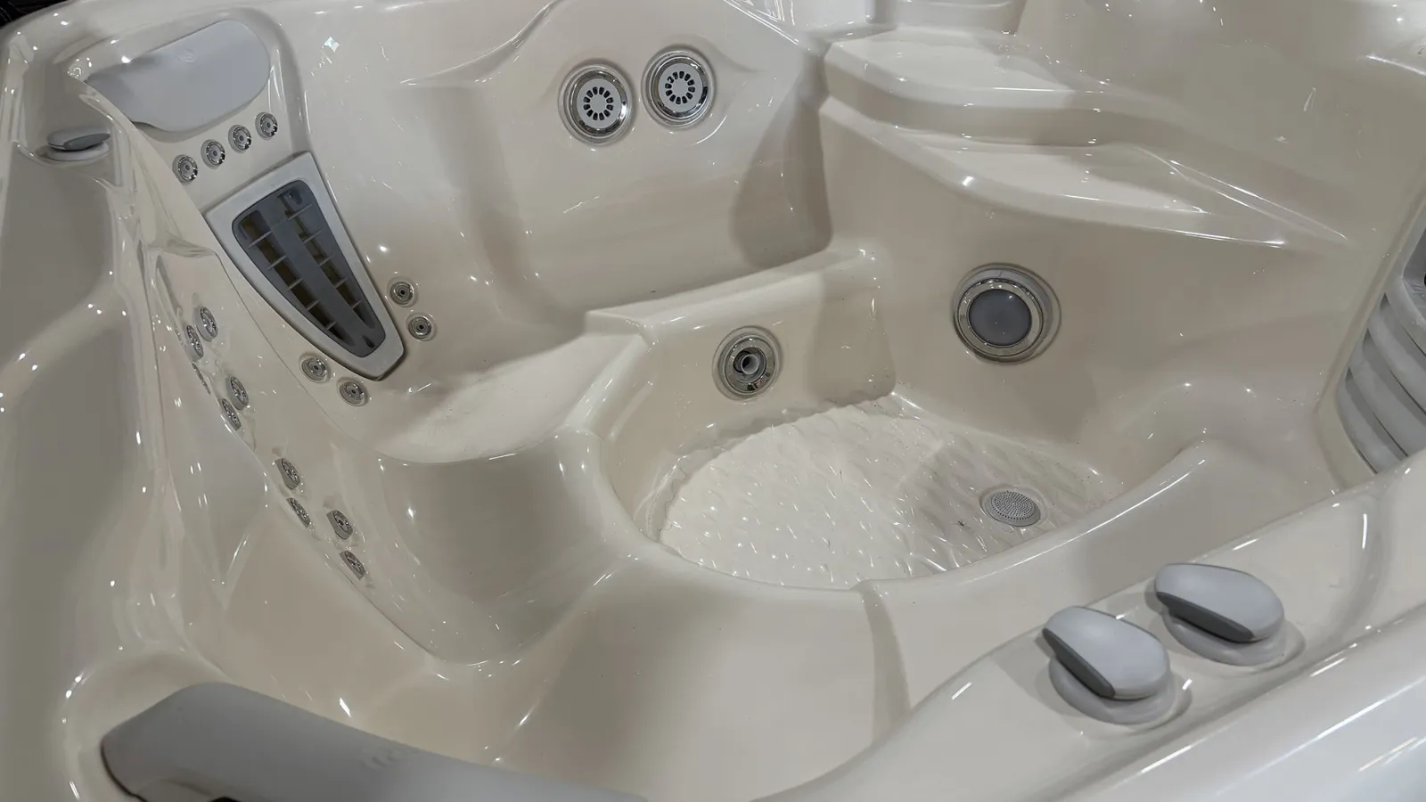 White glossy spa bathtub with multiple jets, seating, and built-in control knobs in a clean bathroom setting.
