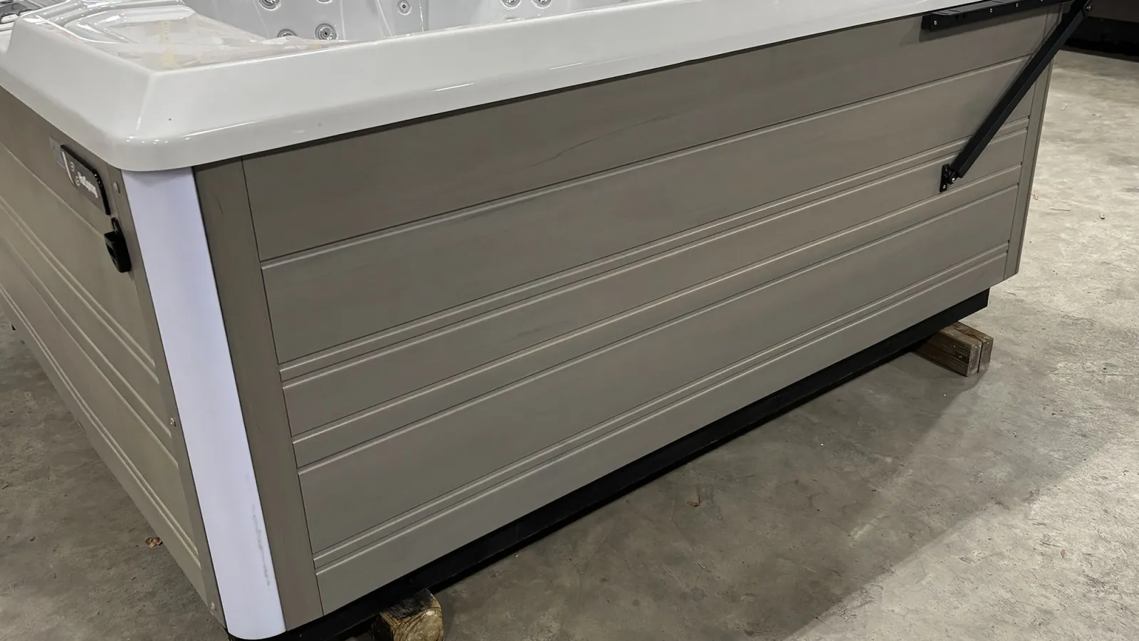 Modern rectangular hot tub with a beige exterior panel and white rim sitting on wooden blocks indoors.