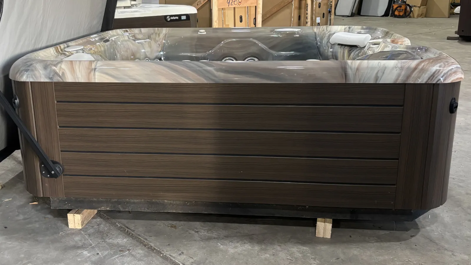 Modern rectangular hot tub with brown wooden exterior and marble-patterned interior in warehouse setting