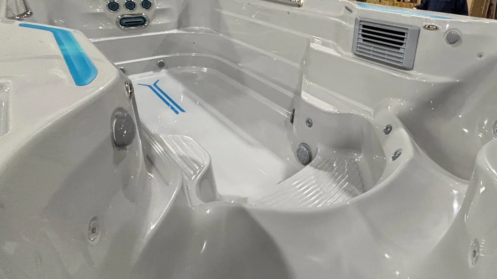 Empty white modern hot tub with built-in seating, jets, and control panel in an indoor setting.