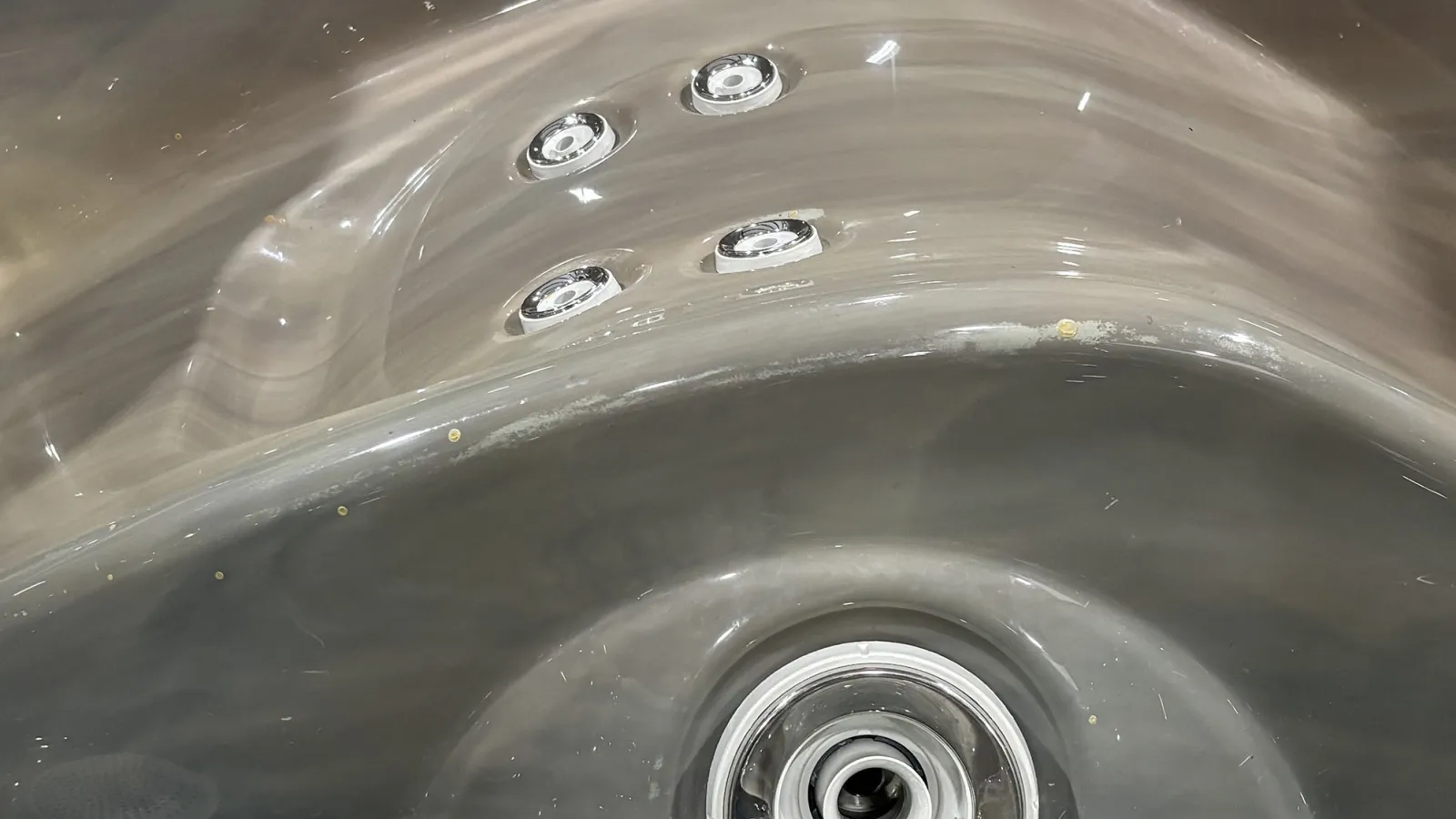 Close-up of a gray jacuzzi tub with four chrome jets and a central drain in a glossy surface.