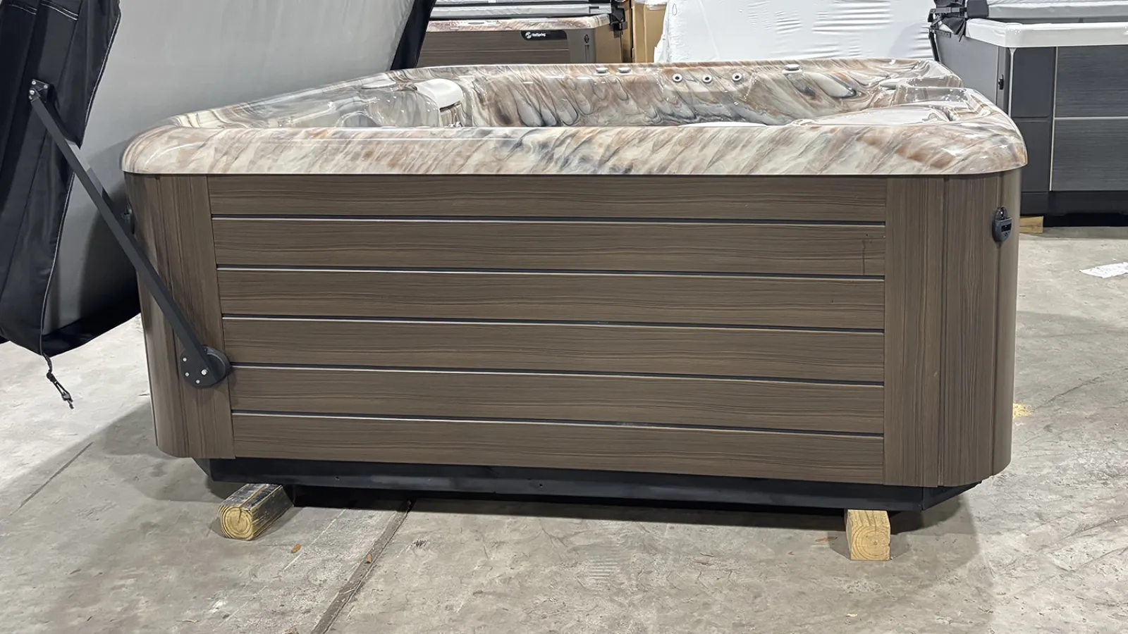 Modern wooden-sided hot tub with marble-patterned interior resting on wooden blocks in a warehouse.