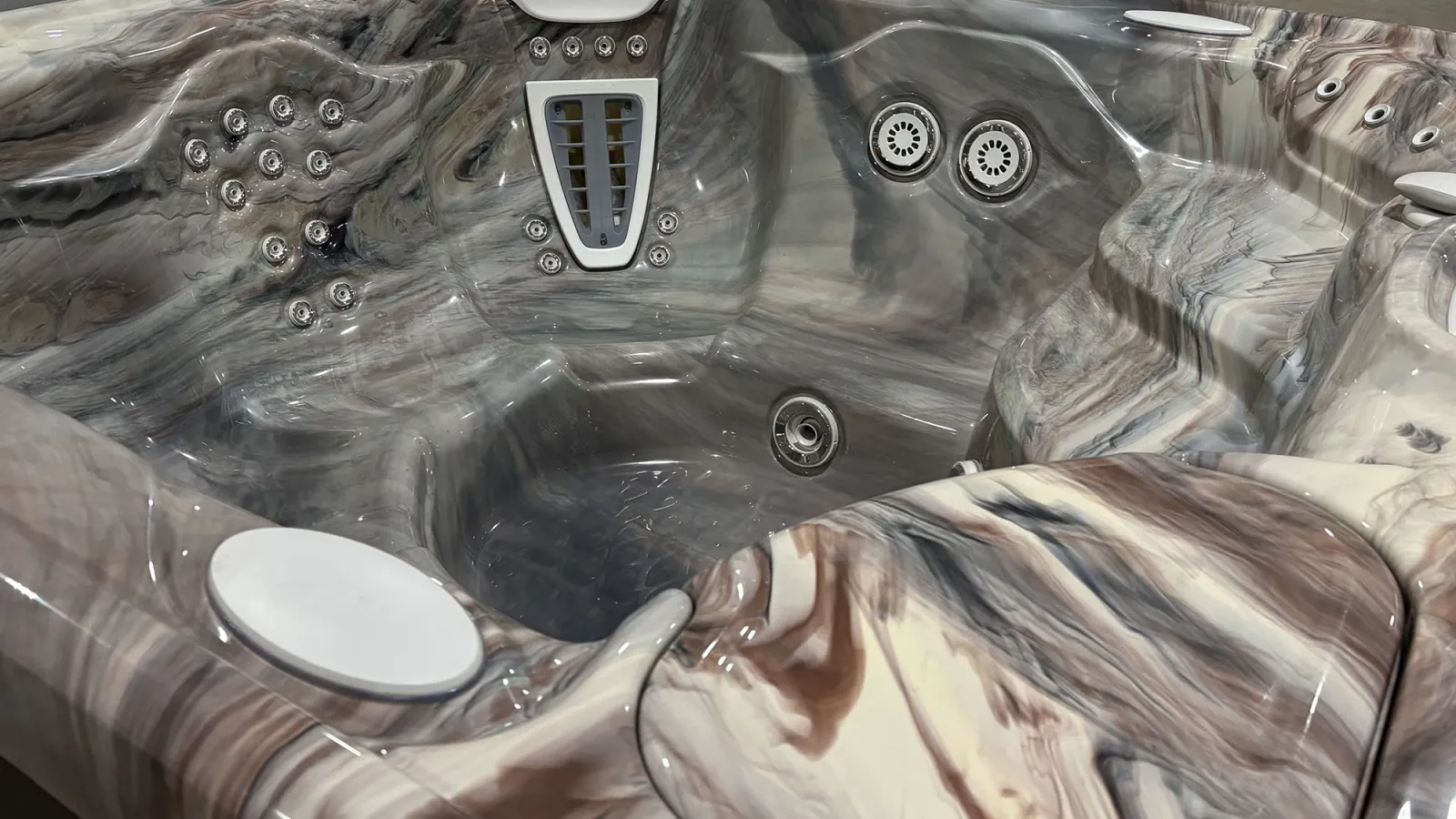 Close-up of empty marble-patterned hot tub with multiple jets and ergonomic seating in glossy finish.