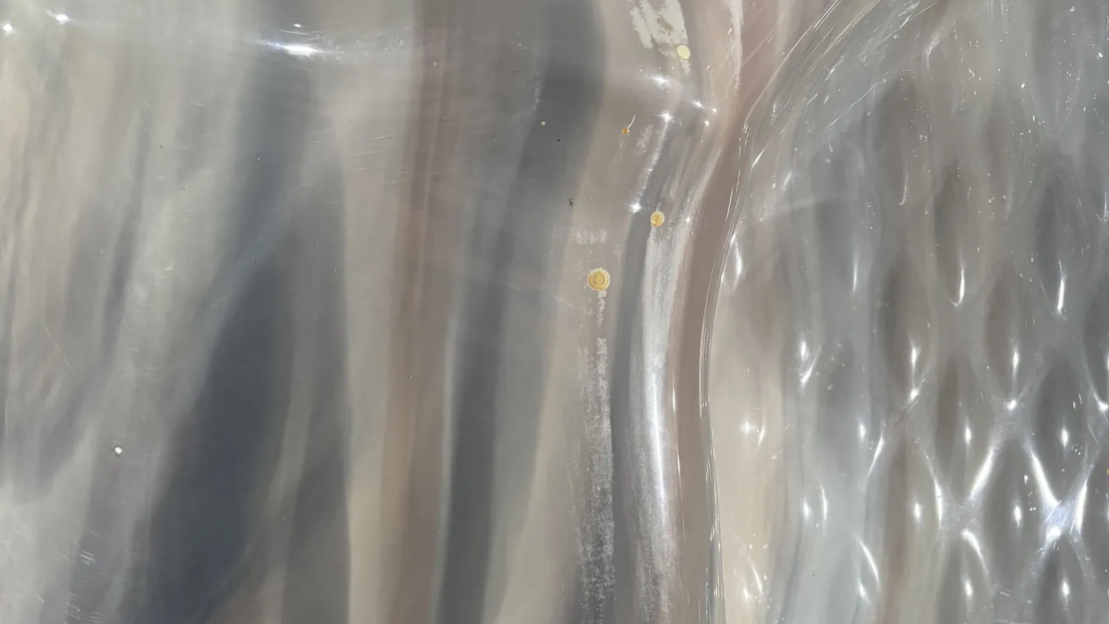 Close-up of translucent, wavy plastic sheet with light reflections and small surface imperfections.