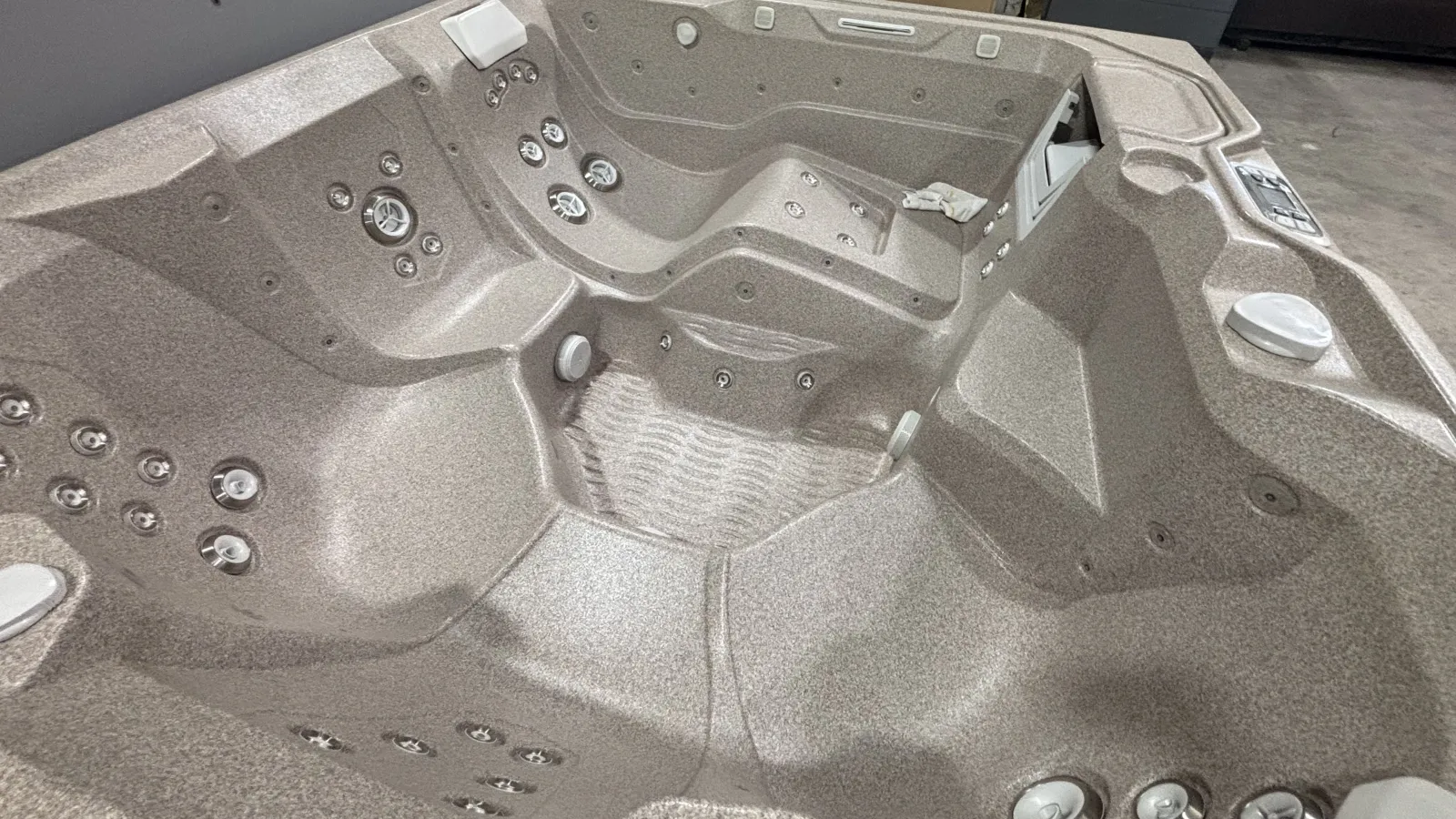 Empty beige spa hot tub with multiple jet nozzles and ergonomic seats in an indoor setting