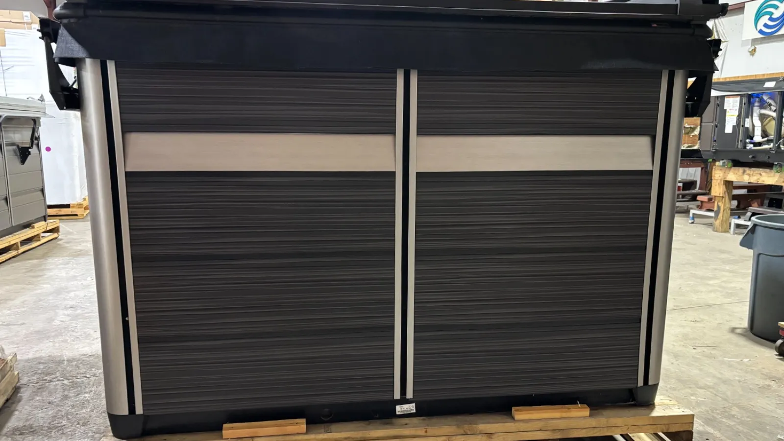 Large black and gray industrial storage container on pallet in warehouse with metal and wood surroundings