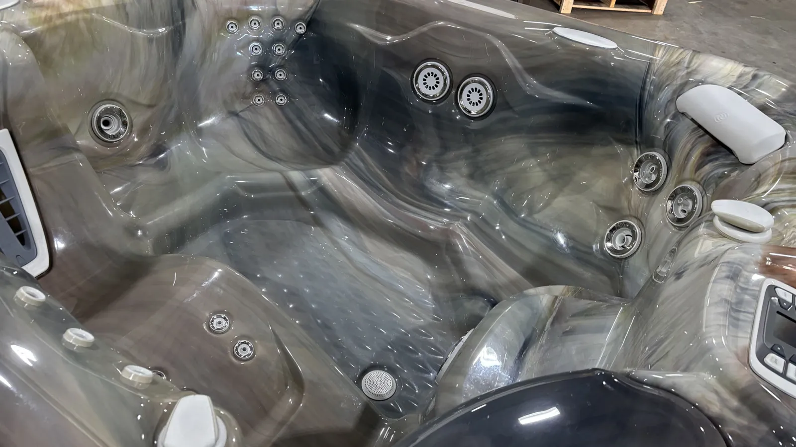 Empty gray marble-patterned hot tub with multiple jets, headrests, and seating areas indoors.