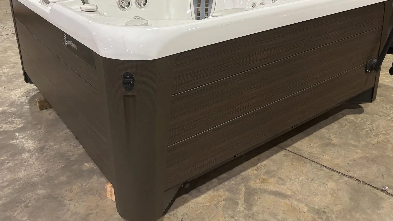 Modern spa hot tub with white acrylic interior and dark wood-style exterior panels, placed on concrete floor.