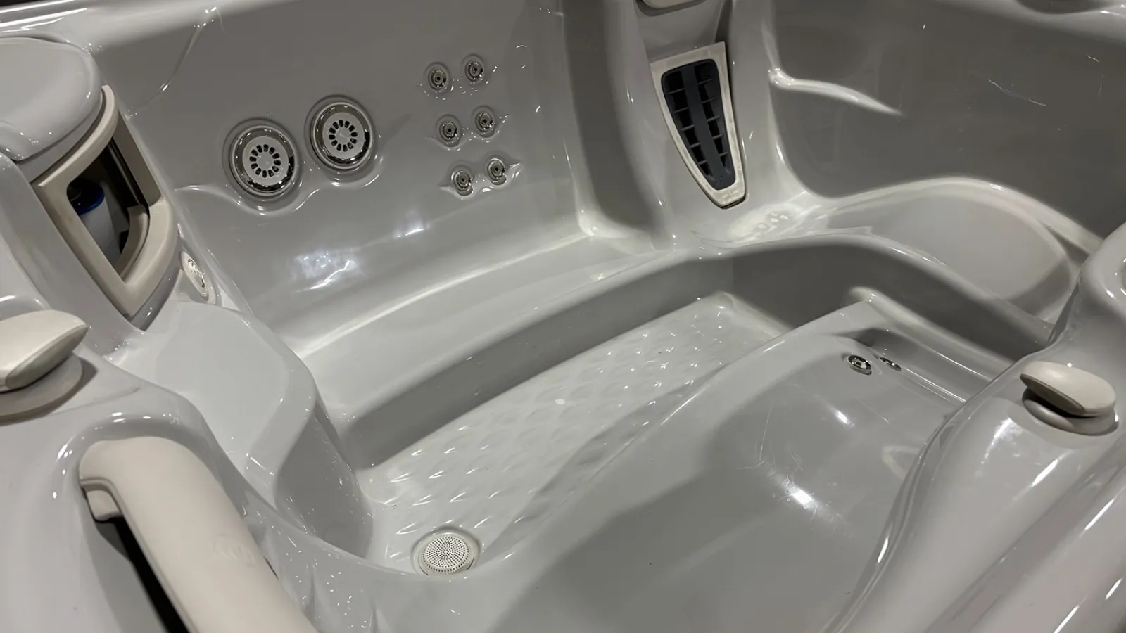 Empty white hot tub interior with multiple water jets and textured seating area under bright lighting